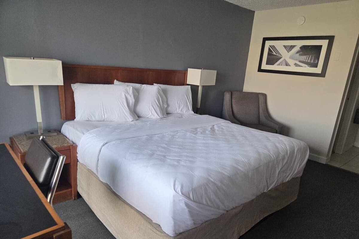 A neatly made bed with white linens, a wooden headboard, and two bedside lamps.
