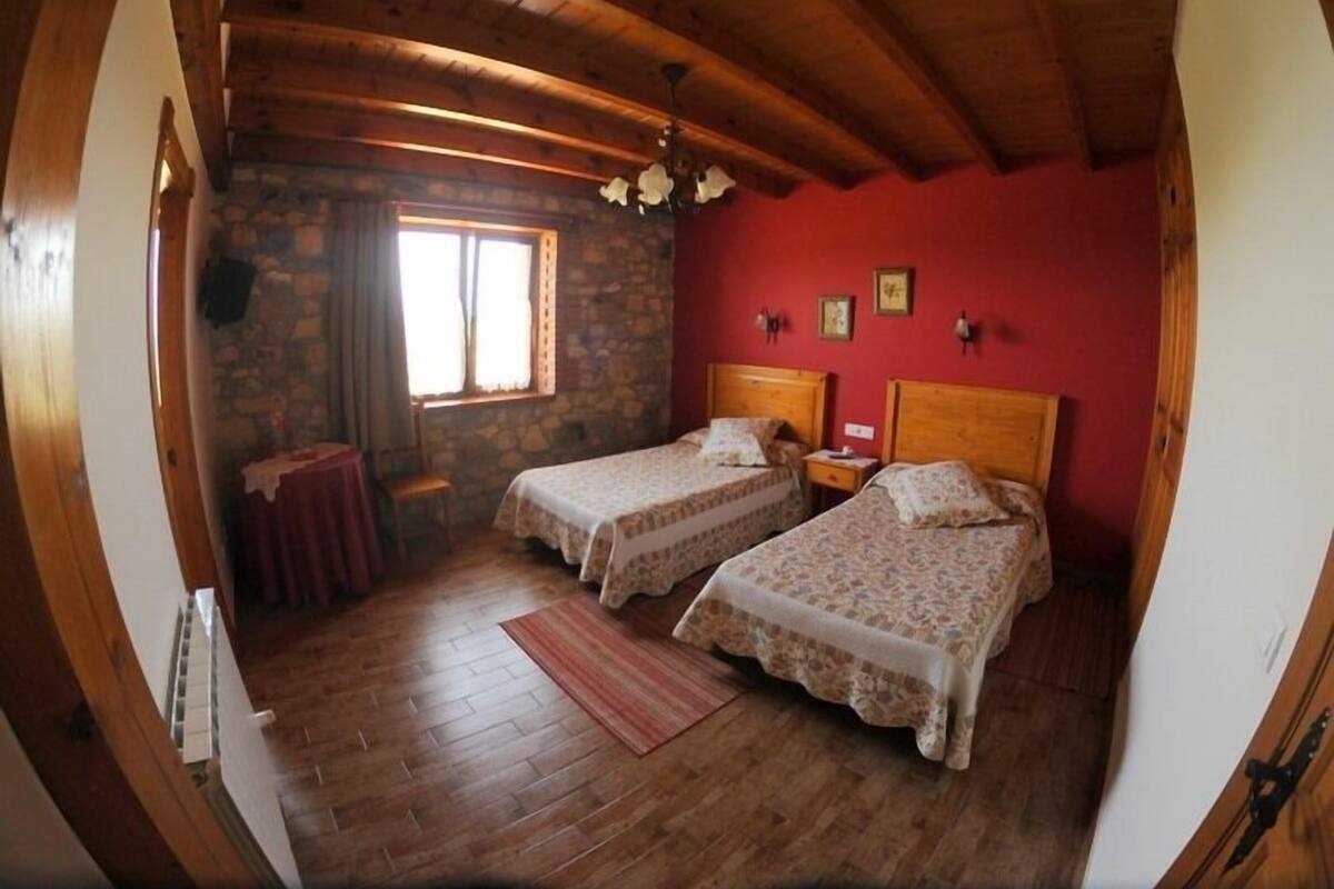 A room with two beds, a stone wall, a wooden ceiling, and a window with curtains.