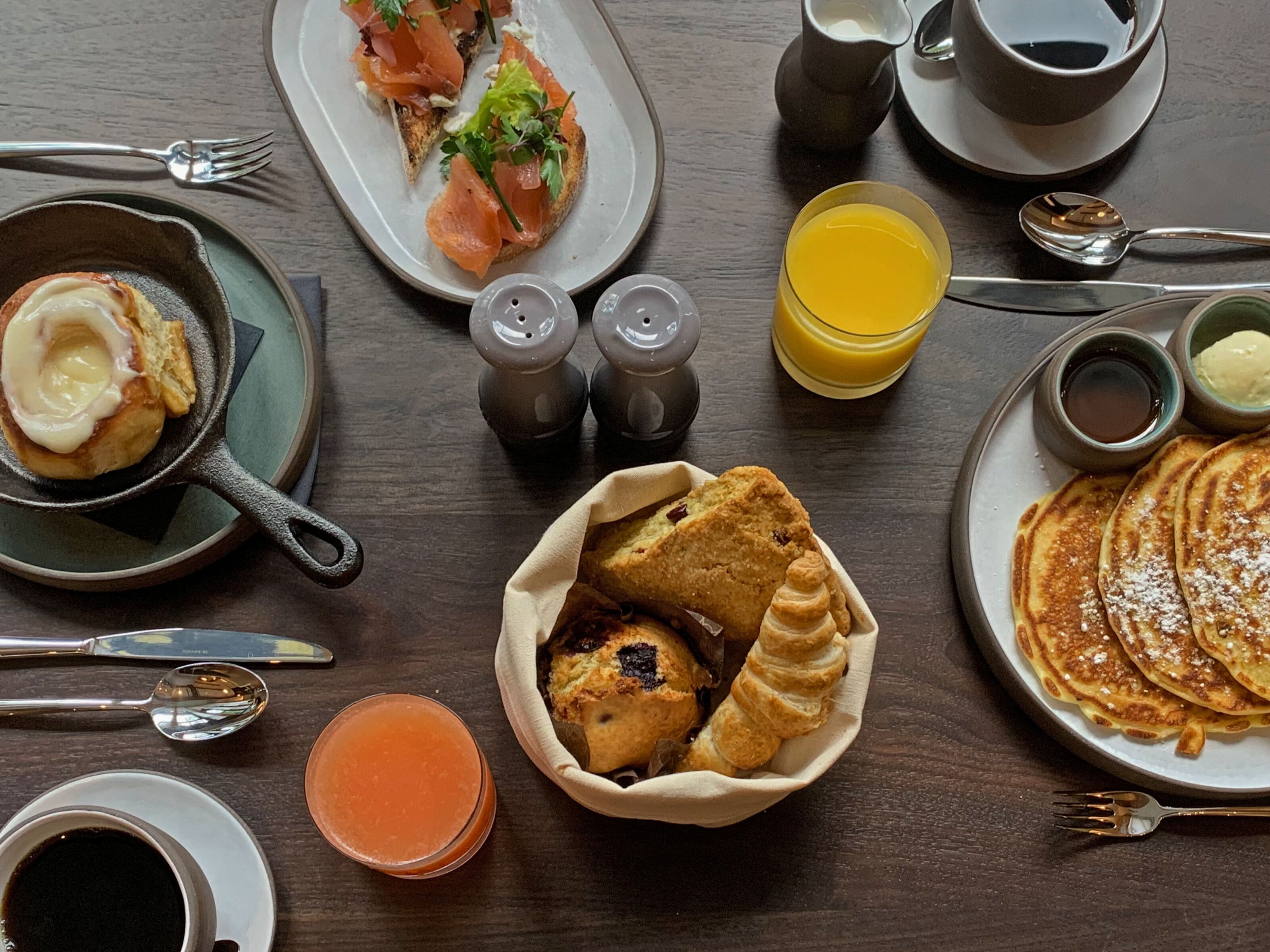 A breakfast setting with various dishes including pancakes, a croissant, and smoked salmon on toast.