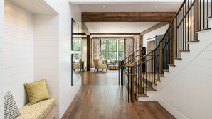 Ambiente spazioso con scala in legno, angolo salotto con cuscini decorati e ampie finestre che lasciano entrare la luce naturale.