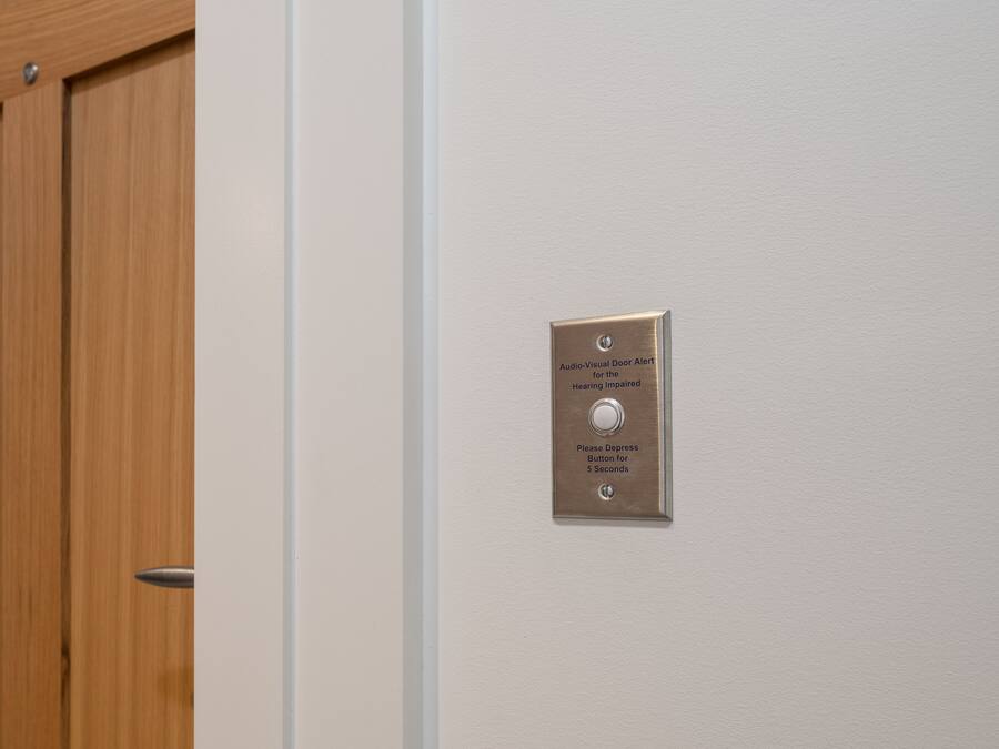 A door with a wooden finish and a metallic plate with instructions for an audio-visual door alert for hearing-impaired individuals.