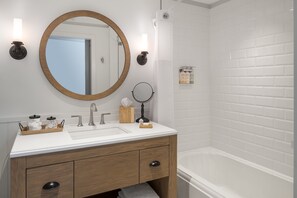 A bathroom with a wooden vanity, a round mirror, a sink, and a bathtub. - The Williams Inn (Williamstown)