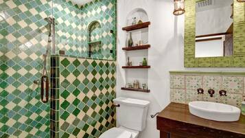 Un baño con un patrón de baldosas blancas y verdes a cuadros, un inodoro blanco, un tocador de madera con un lavamanos blanco y una lámpara colgante.