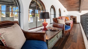 Un patio soleado con sofás de cuero, una mesa de madera y ventanas arqueadas con vistas a una zona residencial.