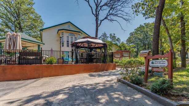 A building with a covered outdoor seating area, a sign indicating a bed and breakfast, and a fenced entrance. - The Whispering Pines Inn Bed & Breakfast (Norman)