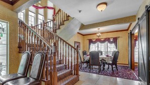 A spacious dining area with a high ceiling, a wooden staircase, and a view of the outdoors. - The Whispering Pines Inn Bed & Breakfast (Norman)
