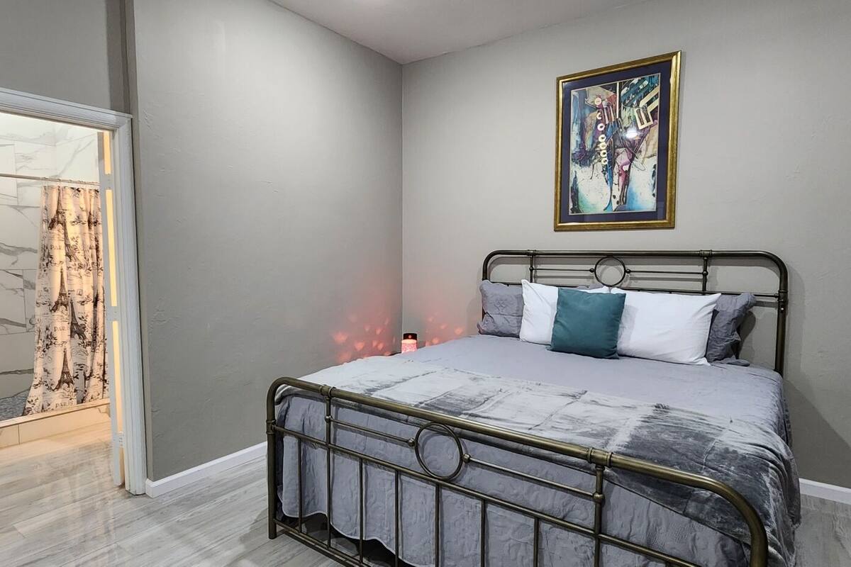 A bedroom with a bed, a nightstand, a painting, and a door leading to a balcony.