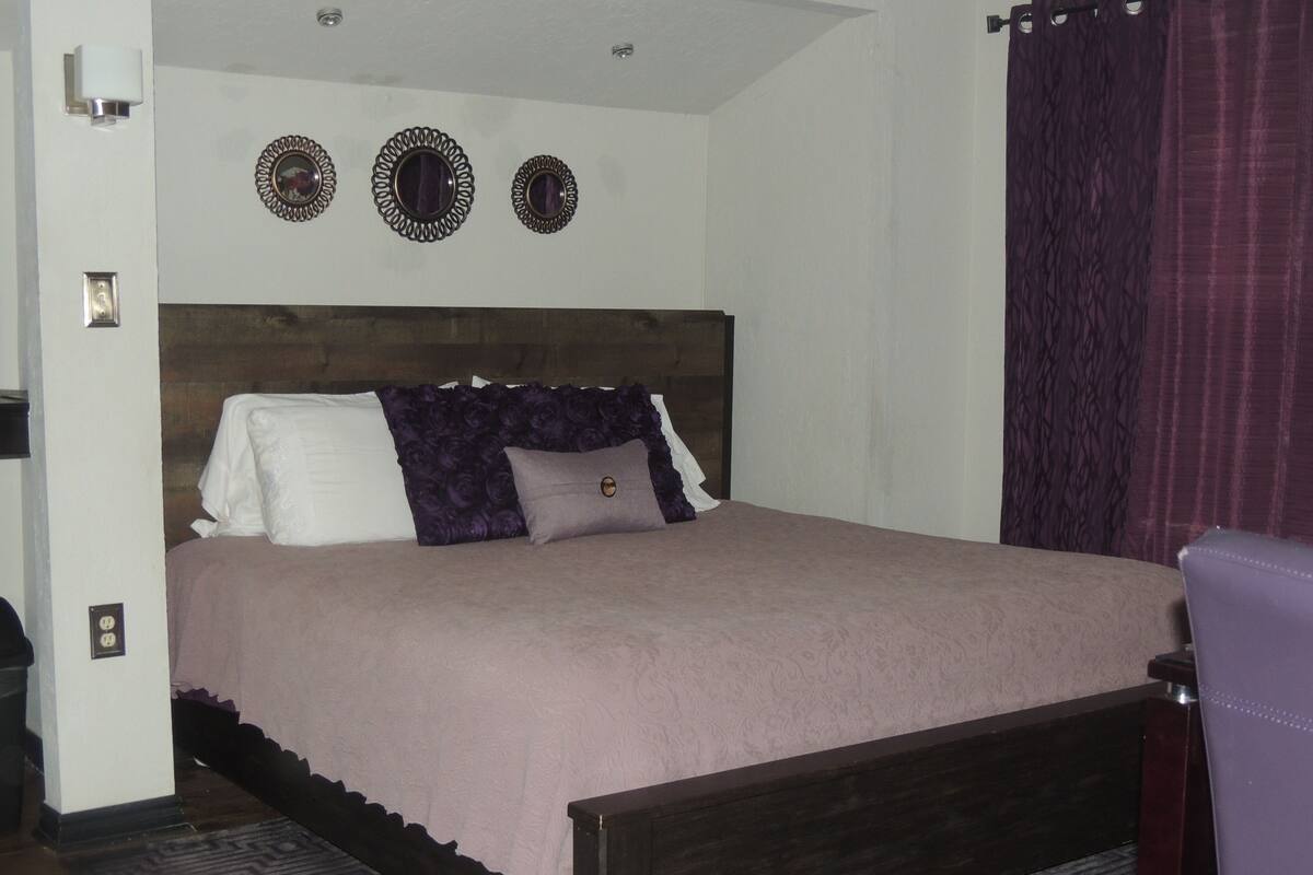 A bedroom with a wooden bed, a headboard, a patterned rug, and a wall-mounted light fixture.
