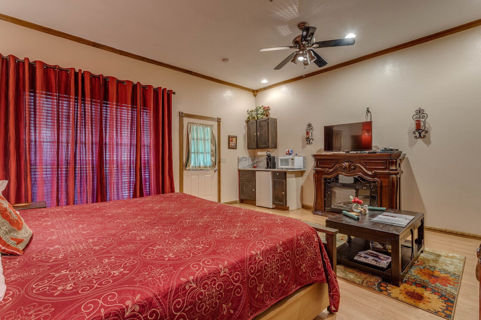 A bedroom with a large bed, a desk with a computer, a television, and a fireplace.