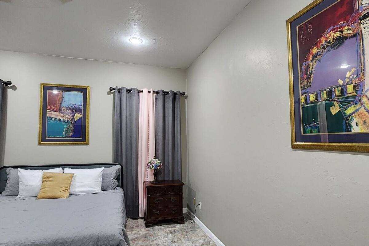 A bedroom with a bed, curtains, a nightstand, and two framed pictures on the wall.