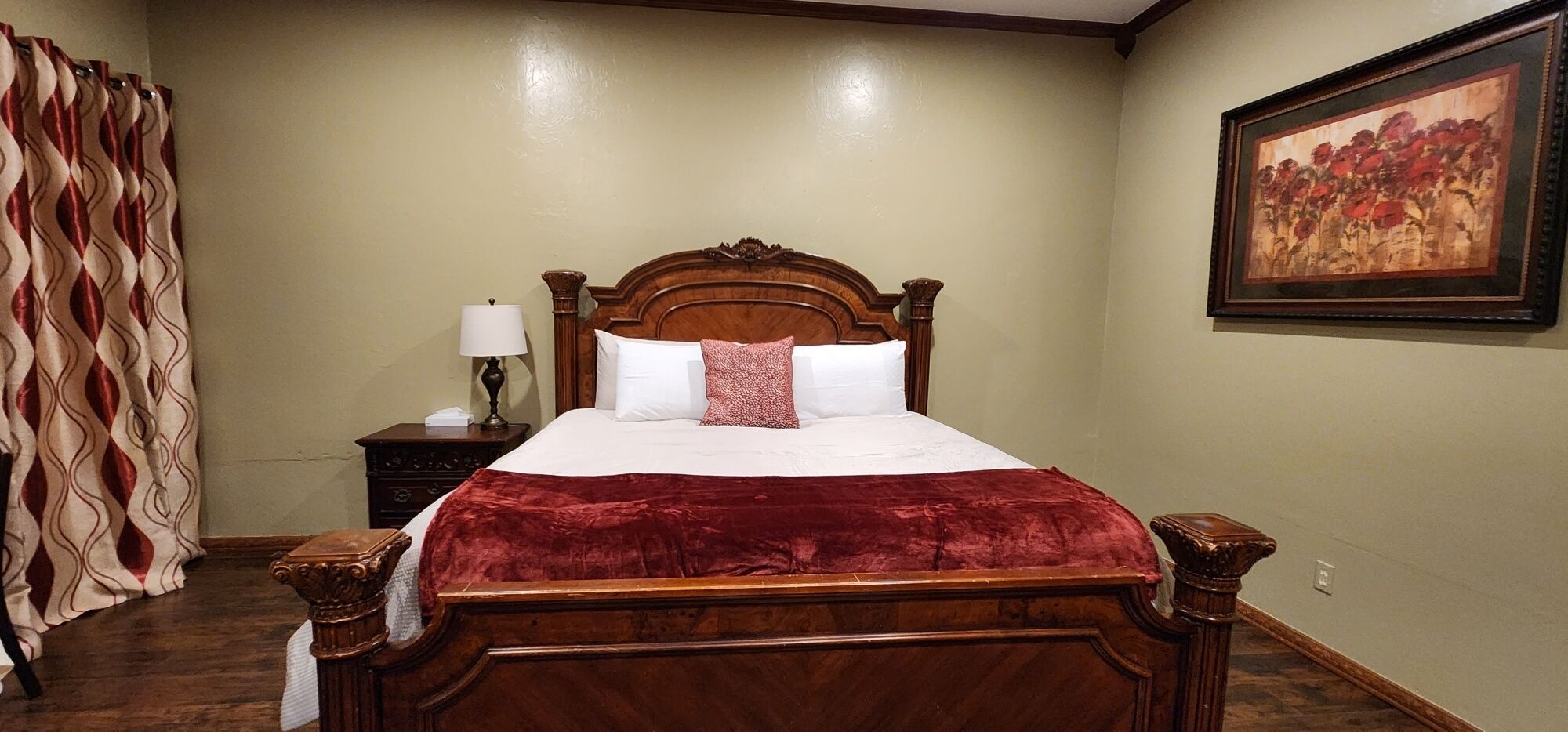 A bedroom with a wooden bed, a nightstand with a lamp, and a wall-mounted painting.
