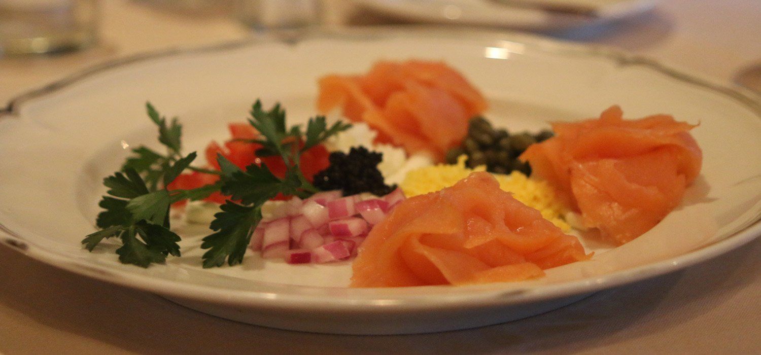 A plate with smoked salmon, diced onions, parsley, and a small amount of black caviar.