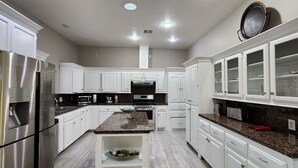 A modern kitchen with white cabinetry, stainless steel appliances, granite countertops, and a central island. - The Whispering Pines Inn Bed & Breakfast (Norman)
