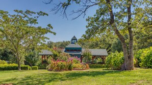 A traditional building with a green roof and a central tower, surrounded by a well-maintained garden with various plants and a gazebo. - The Whispering Pines Inn Bed & Breakfast (Norman)