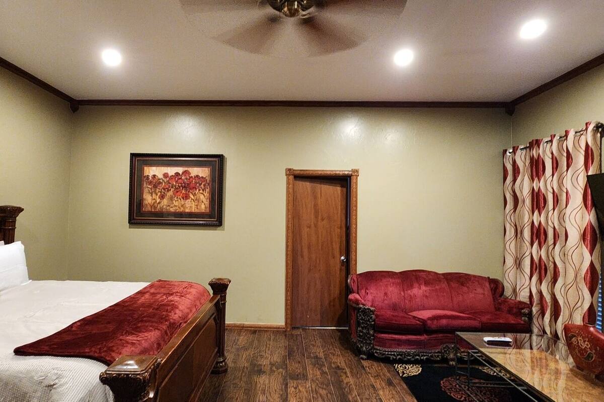 A bedroom with a bed, a red armchair, a wooden door, and a painting on the wall.