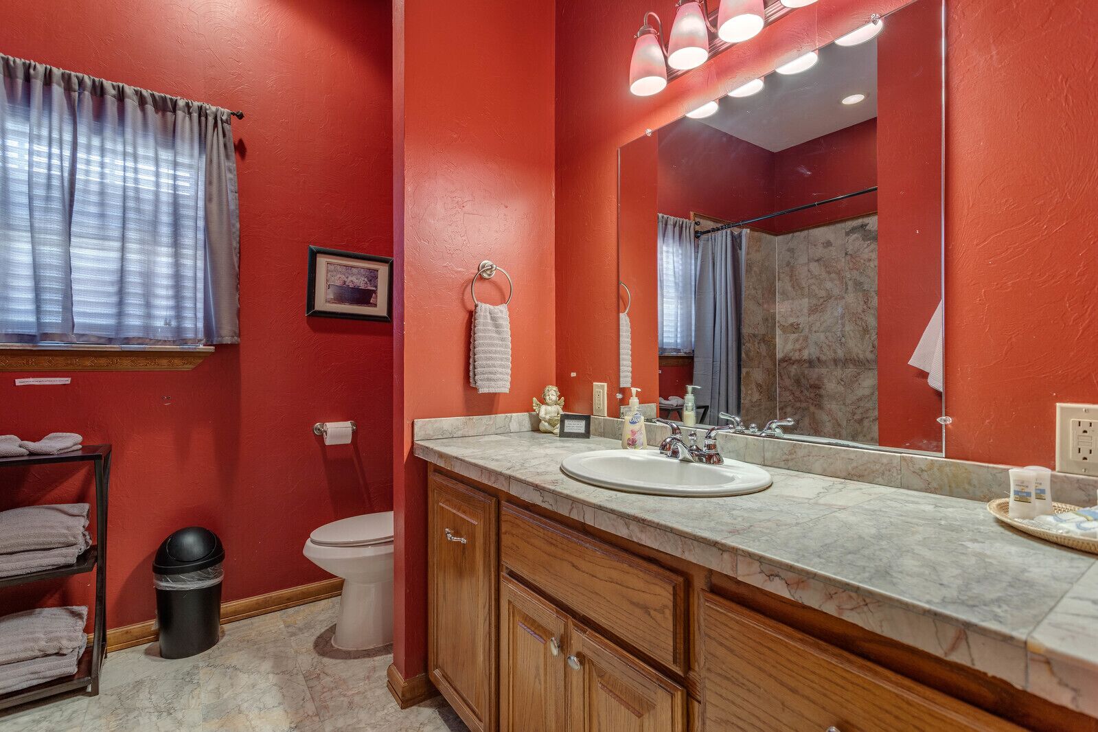 Ein Badezimmer mit roter Wand, einem weißen Waschbecken, Holzschränken, einem Spiegel und einer Toilette.