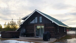 A log cabin with a sloped roof, a glass door entrance, and a small deck area. - Woodhouse Cottages and Ranch (Prince George)