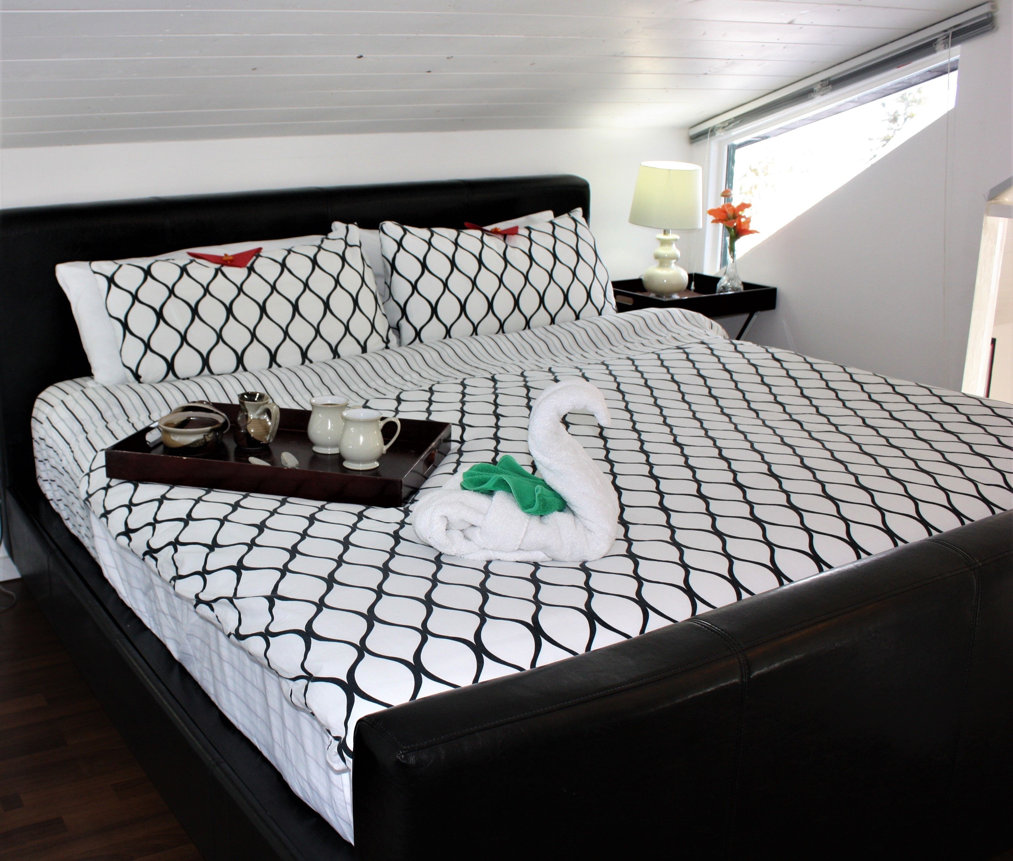 A neatly made bed with a patterned bedspread, a tray with tea cups and a teapot, and a swan-shaped towel.