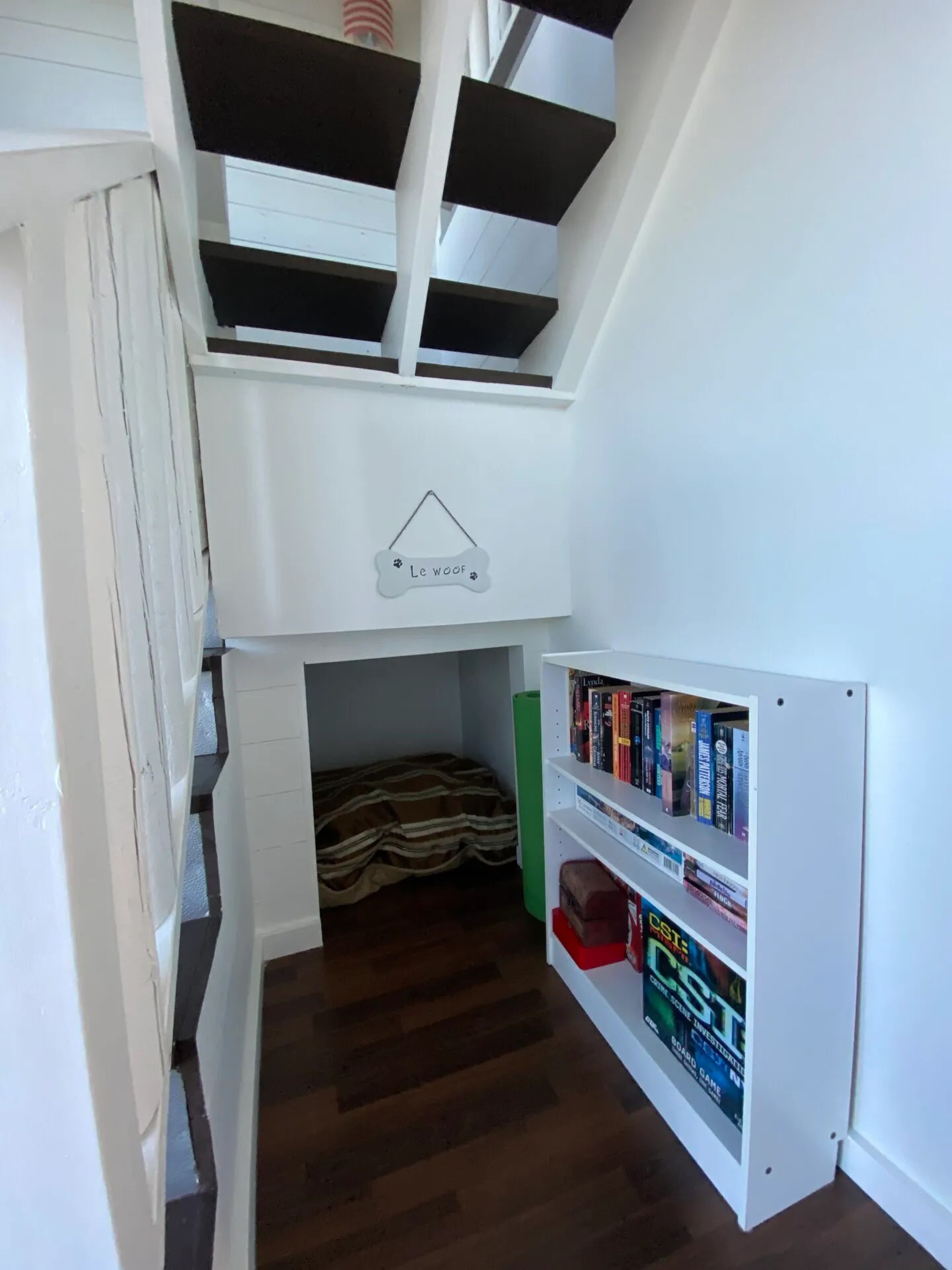 A compact room with a loft bed, a small enclosed sleeping area, and a bookshelf with books and a board game.
