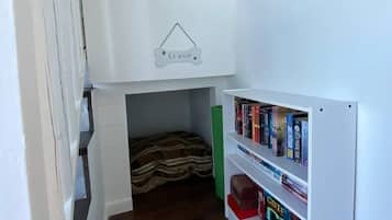Une pièce compacte avec un lit en mezzanine, un petit espace de couchage fermé et une bibliothèque contenant des livres et un jeu de société.