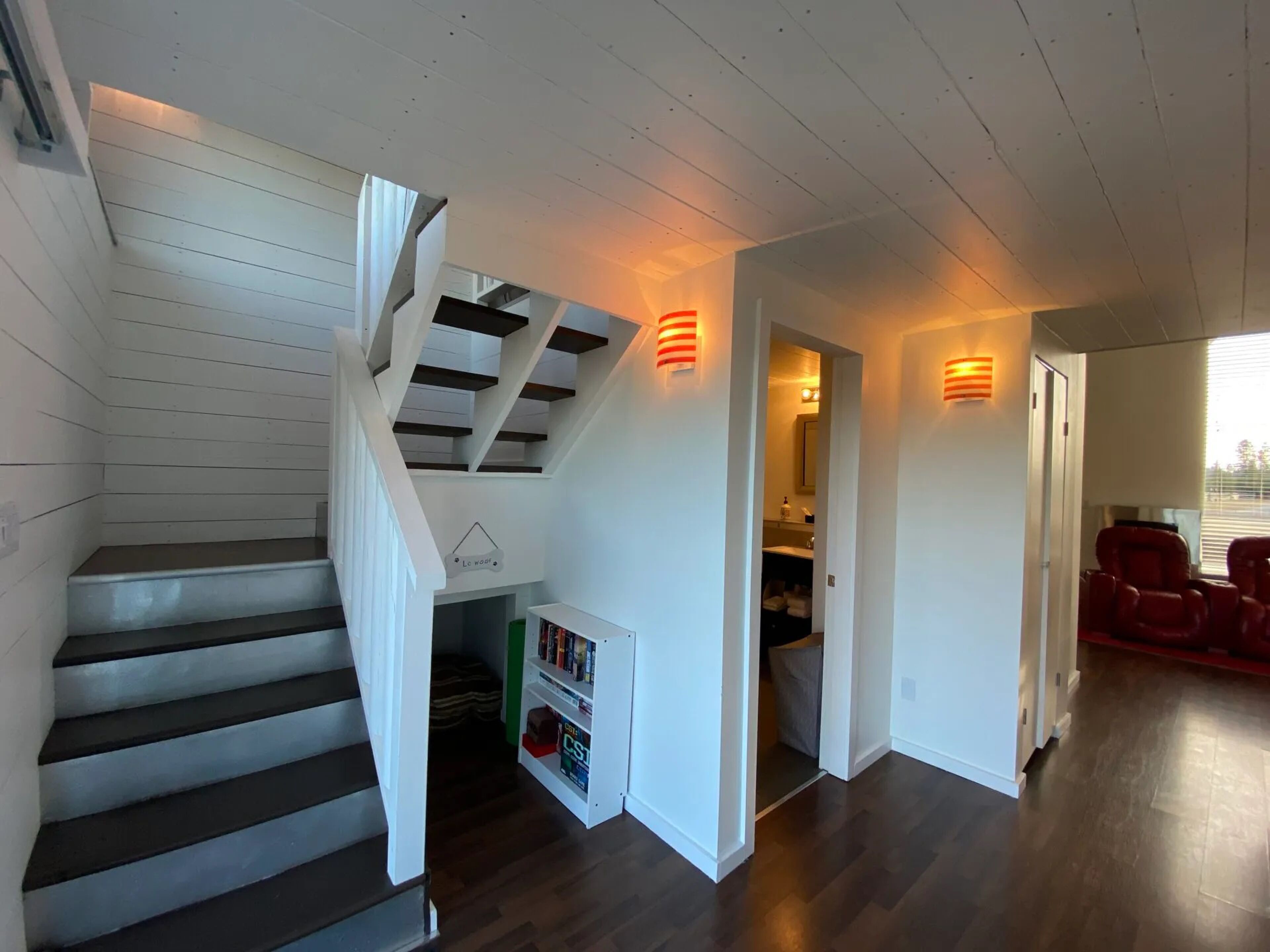 Una escalera con barandillas blancas y peldaños oscuros que conduce a una habitación con una estantería y una puerta.