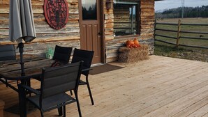 A rustic cabin with a wooden deck, a dining table with chairs, and a door with a window. - Woodhouse Cottages and Ranch (Prince George)