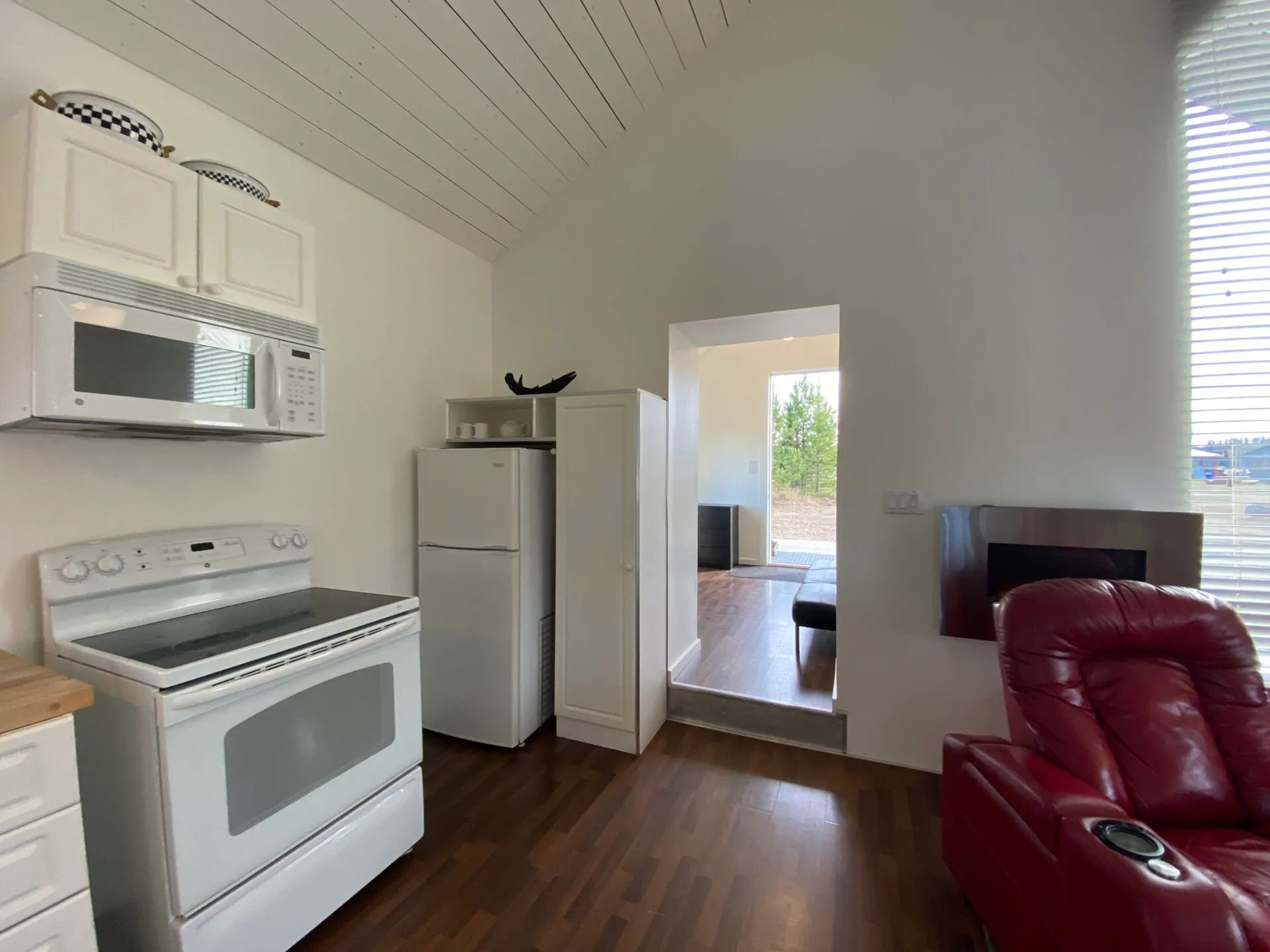 Une cuisine moderne avec des appareils électroménagers blancs, un plancher en bois et un fauteuil en cuir rouge.