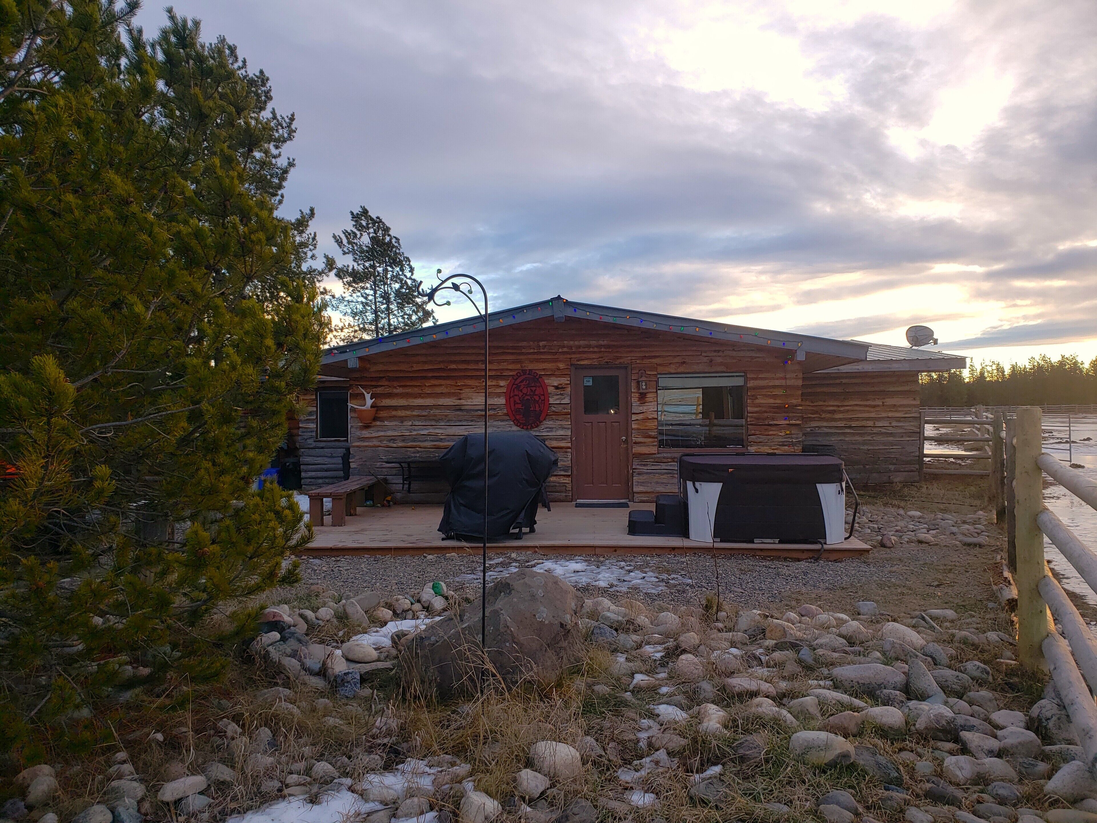 Una cabaña rústica con fachada de madera, una puerta, un ventanal y una parrilla en primer plano.