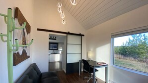 A modern interior with a sofa, desk, and a view of a kitchen and outdoor area. - Woodhouse Cottages and Ranch (Prince George)