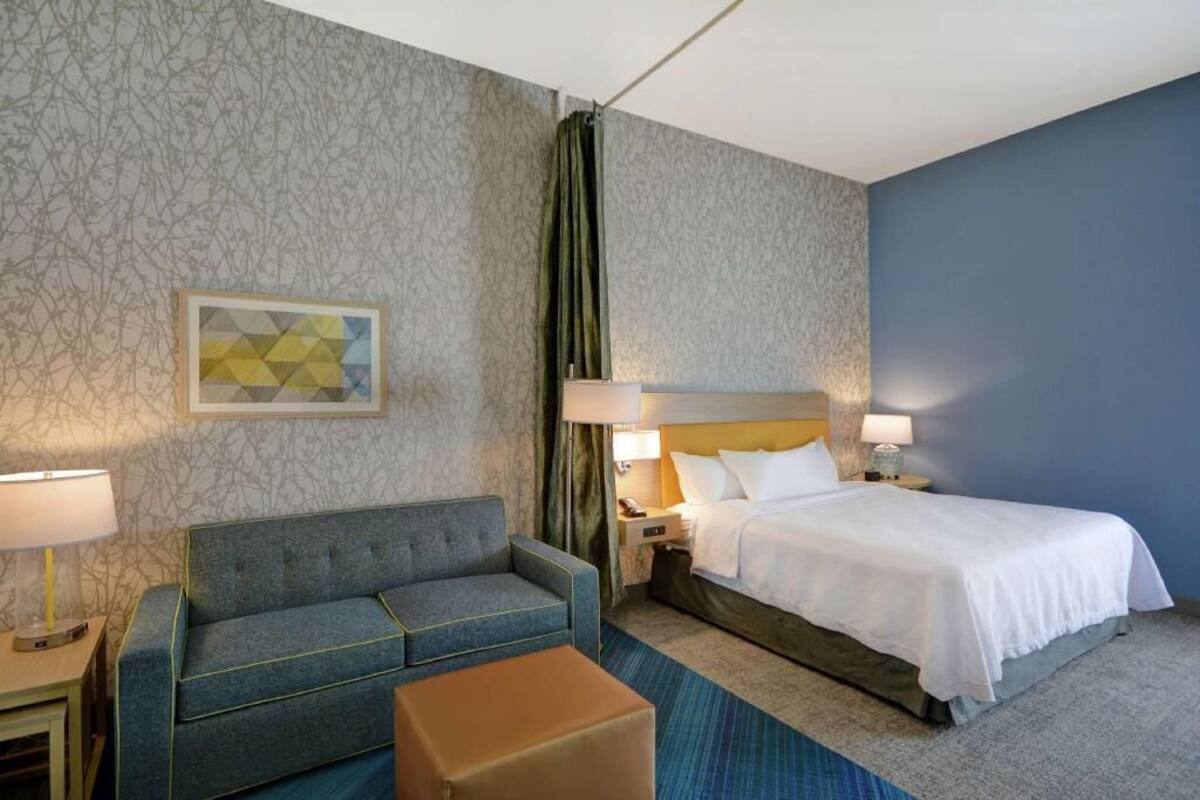Une chambre d’hôtel avec un lit, un canapé, une table de chevet, une lampe et un tableau au mur.
