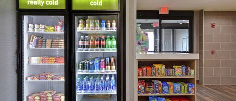 Dois dosadores de bebidas refrigeradas, identificados como 'bem gelado' e 'gelado', com prateleiras repletas de diversas bebidas e lanches.