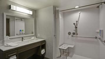 A modern bathroom with a double sink vanity, a large mirror, a shower with a handheld showerhead, and a small stool.