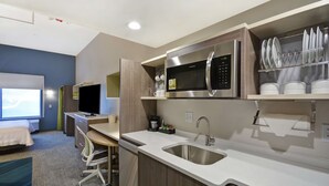 A compact hotel room with a kitchenette, a bed, a desk, and a TV.