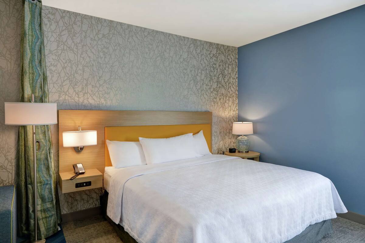 Une chambre d’hôtel avec un grand lit, deux tables de chevet avec des lampes, un téléphone et un papier peint à motifs.