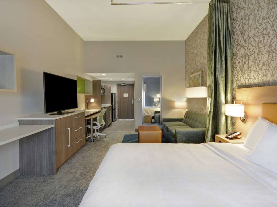 A hotel room with a bed, desk, television, and a view into the hallway.