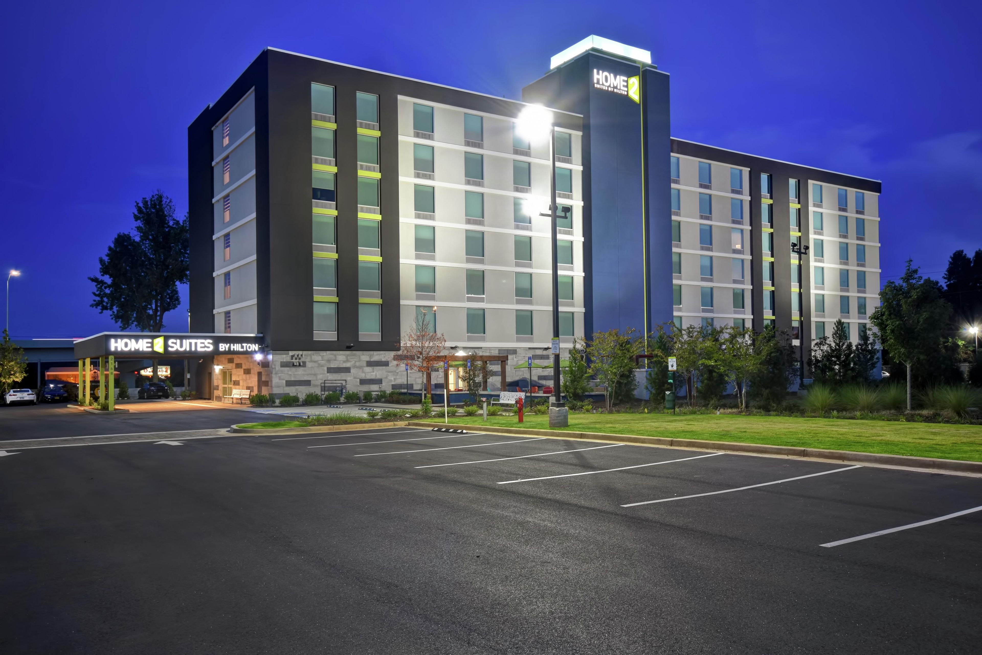 Un hotel de varios pisos con un cartel llamativo de 'HOME SUITES BY HILTON' y un estacionamiento bien iluminado.