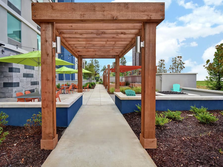 A covered outdoor seating area with tables and chairs, a concrete pathway, and a building with a stone facade.