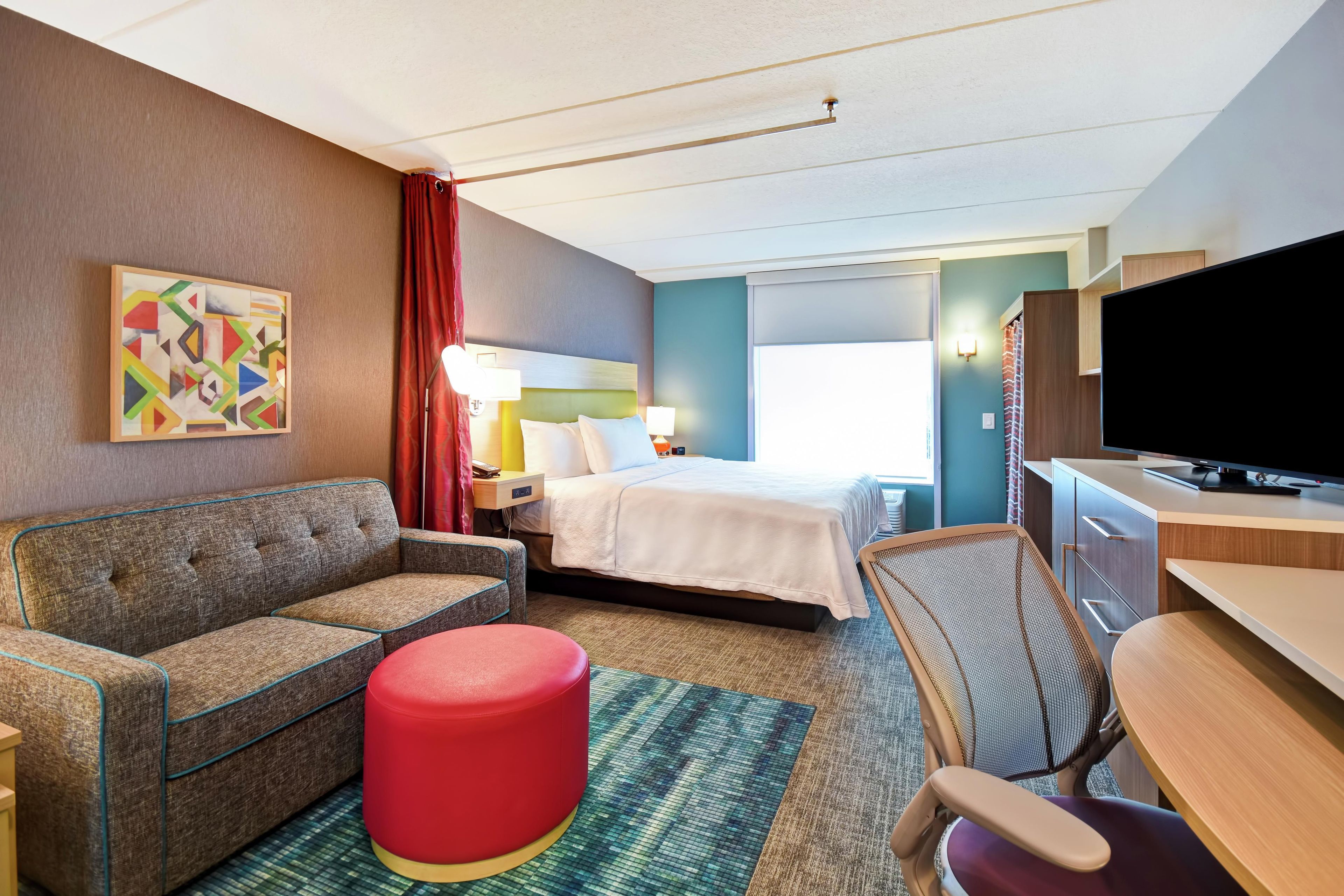 Habitación de hotel con cama, sofá, escritorio, televisor y un cuadro en la pared.