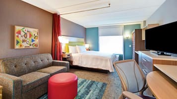 Habitación de hotel con cama, sofá, escritorio, televisor y un cuadro en la pared.
