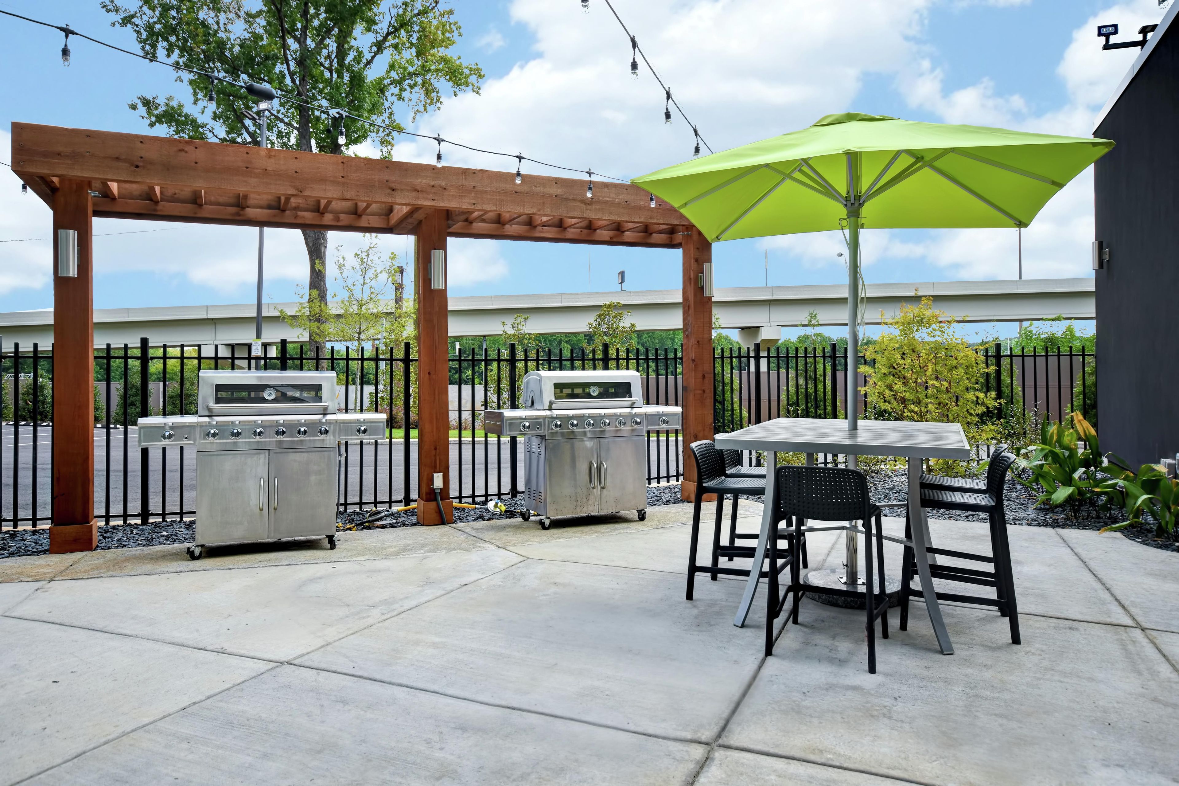 An outdoor patio with two barbecue grills, a pergola, and a table with chairs.