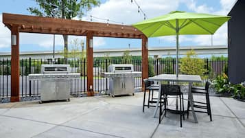 An outdoor patio with two barbecue grills, a pergola, and a table with chairs.