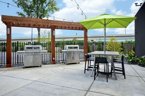 Un patio exterior con dos parrillas, una pérgola y una mesa con sillas.