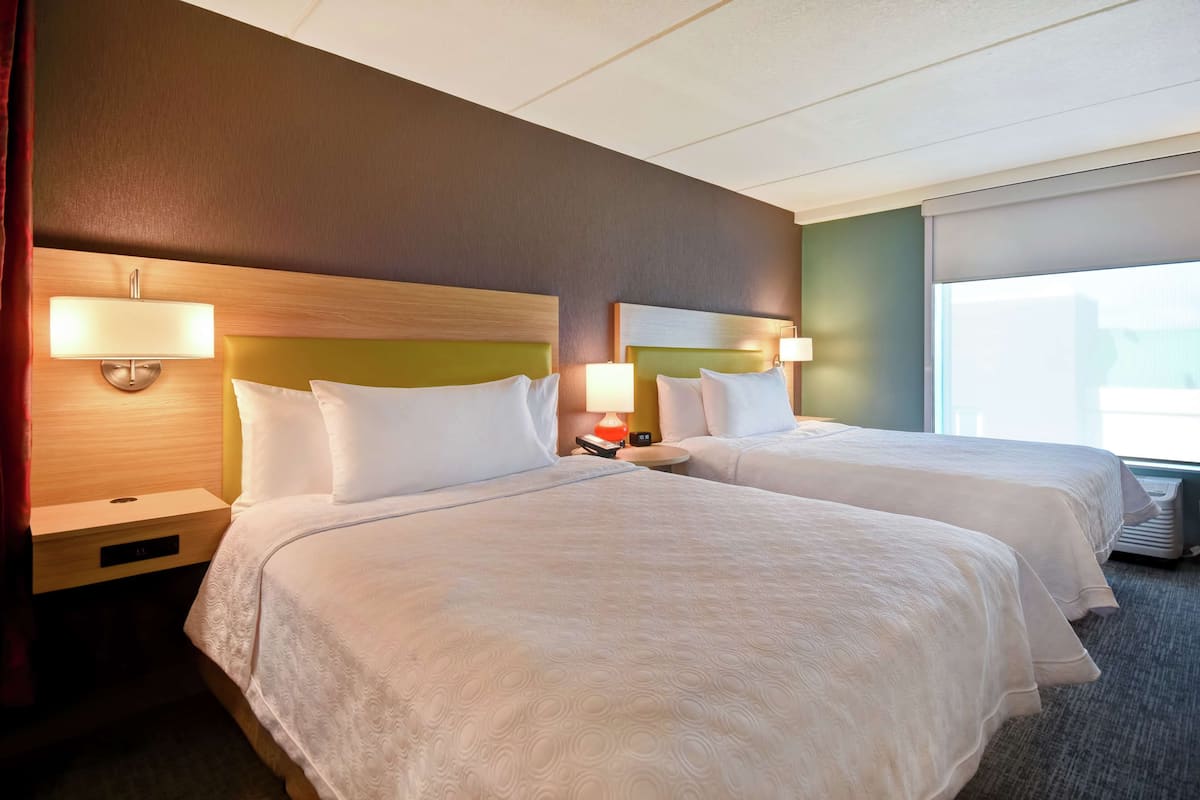 Une chambre d’hôtel avec deux lits, chacun doté d’une tête de lit, de lampes de chevet et d’une table de chevet.