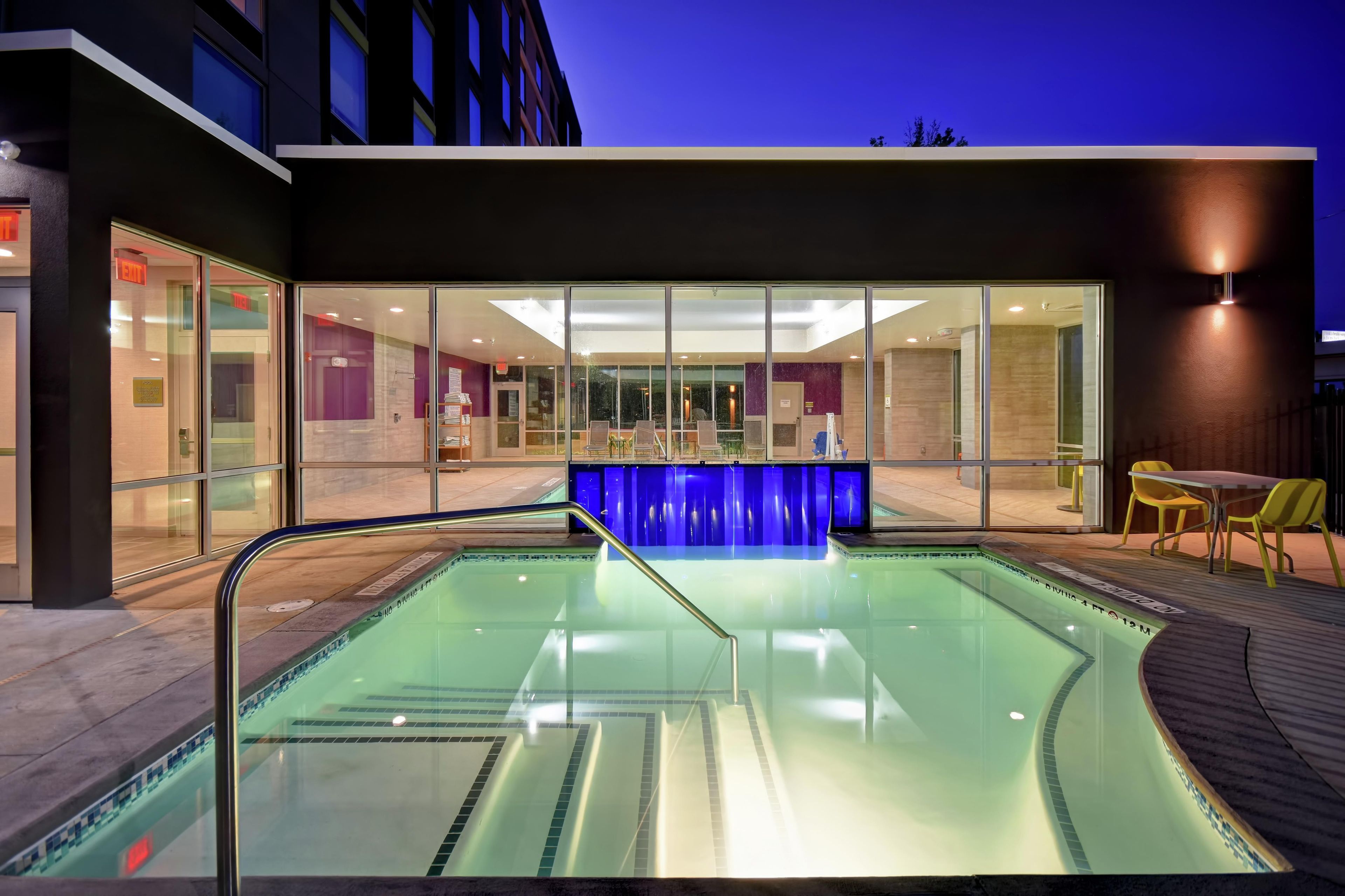 A swimming pool with a glass barrier, indoor seating area, and a modern building facade.