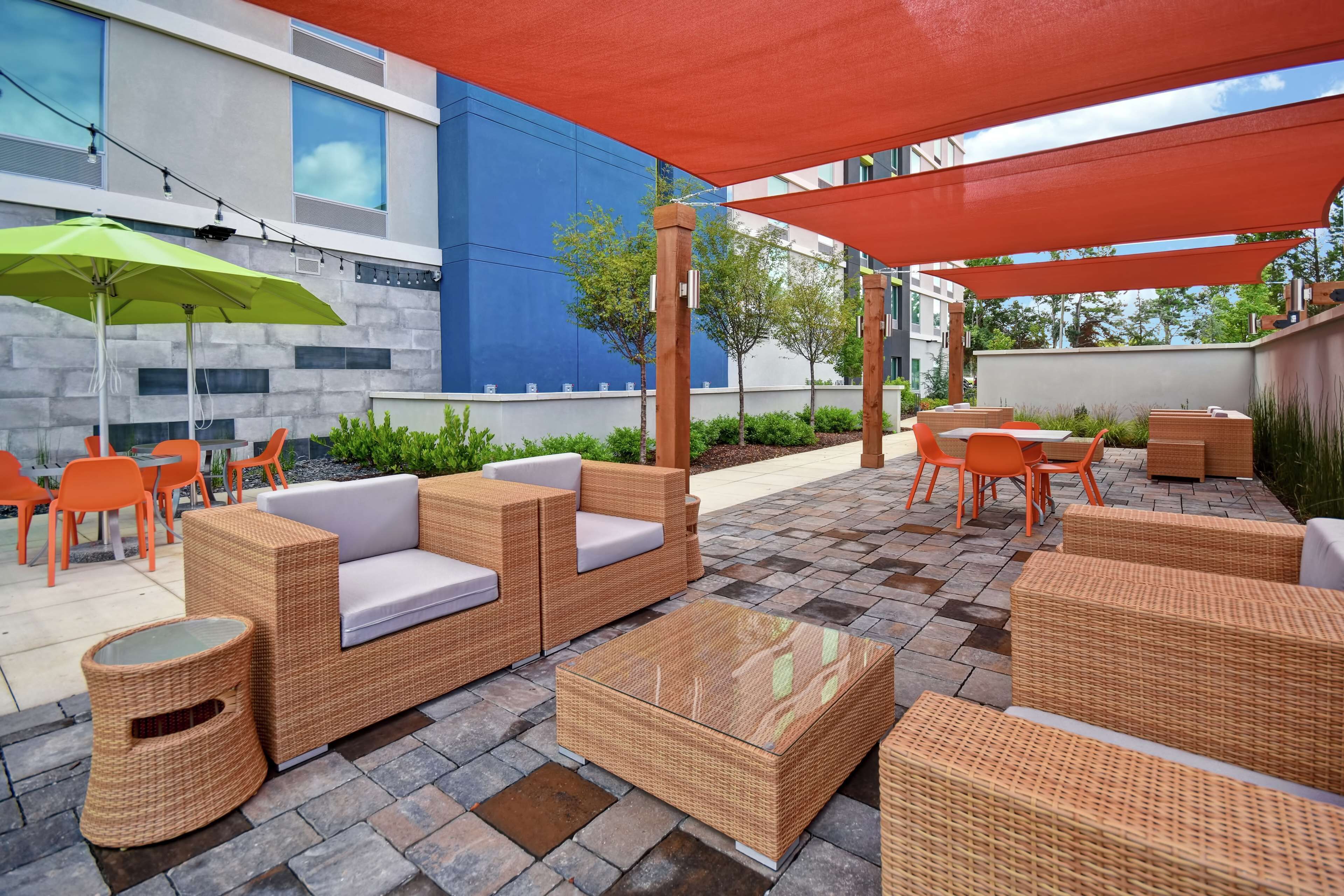 Un patio al aire libre con mobiliario de mimbre, un parasol verde y sillas naranjas.