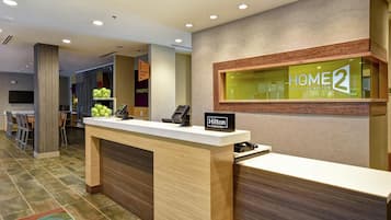 A hotel reception desk with a 'Home2' sign, a 'Hilton Honors' sign, and a 'Conserve' sign.