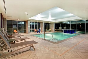 Piscina interior moderna con sillones de descanso, terraza soleada y ventanas amplias.