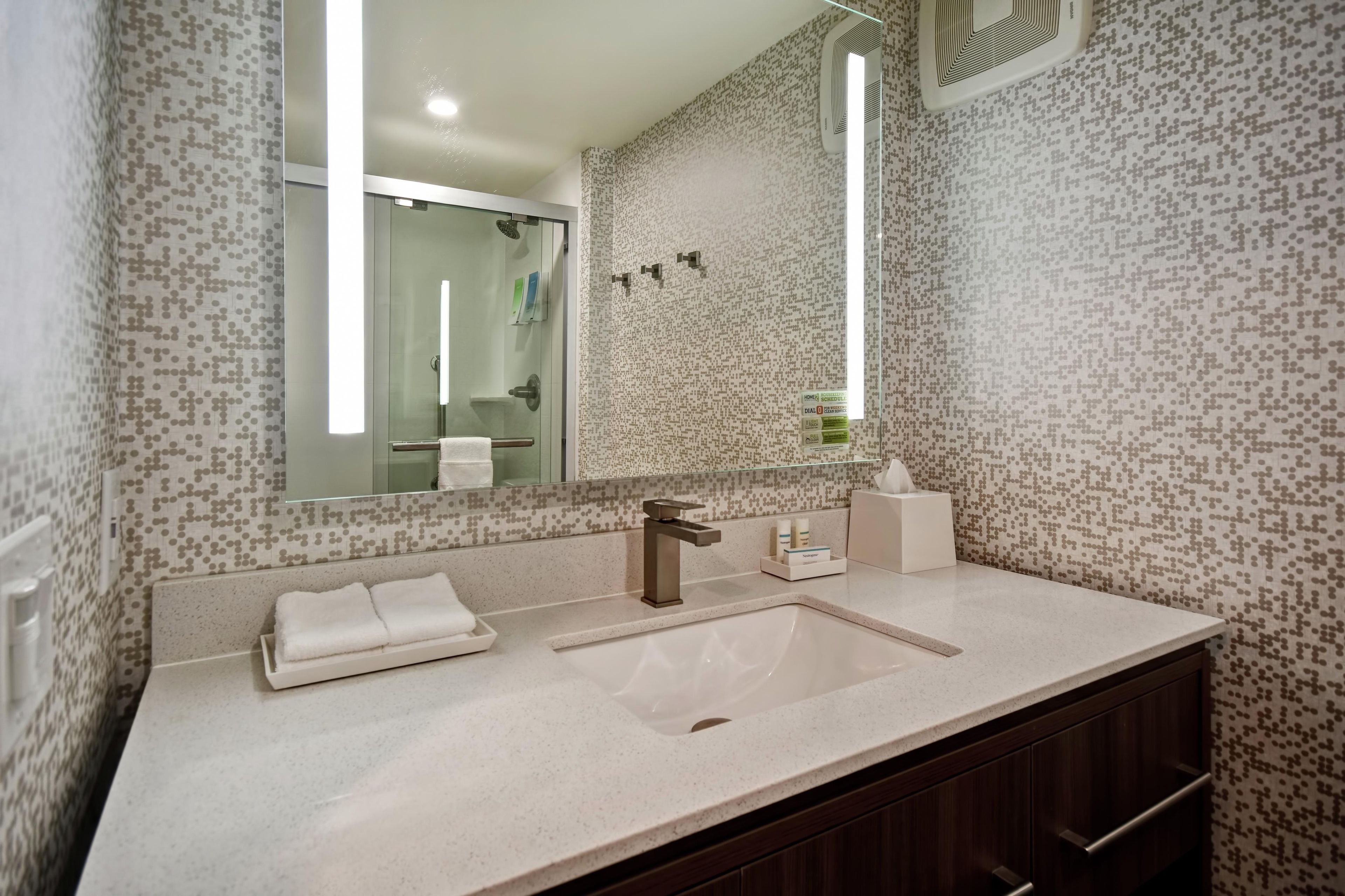 Un baño con un espejo grande, un lavabo y un perchero para toallas.