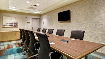 Un salón de conferencias con una larga mesa, múltiples sillas, un televisor de pantalla plana y un cuadro en la pared.