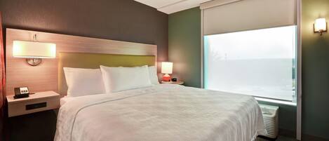 Una habitación de hotel con una cama, mesitas de noche, lámpara y una ventana con persianas.